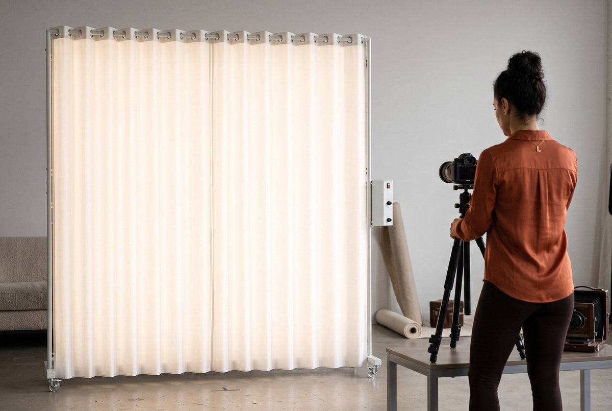 Lucy, a photographer, adjusting a camera tripod in front of a glowing LEDWindow PRO window-style LED light in a studio